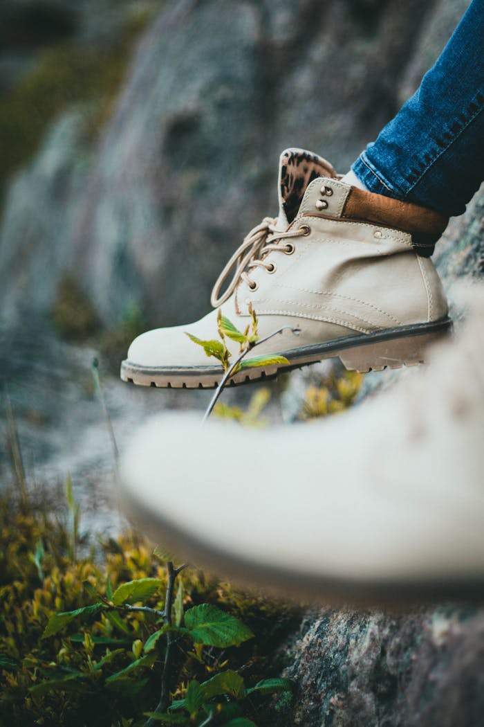 Close-up of beige hiking boots on a rocky surface with greenery. Perfect for outdoor and adventure themes.